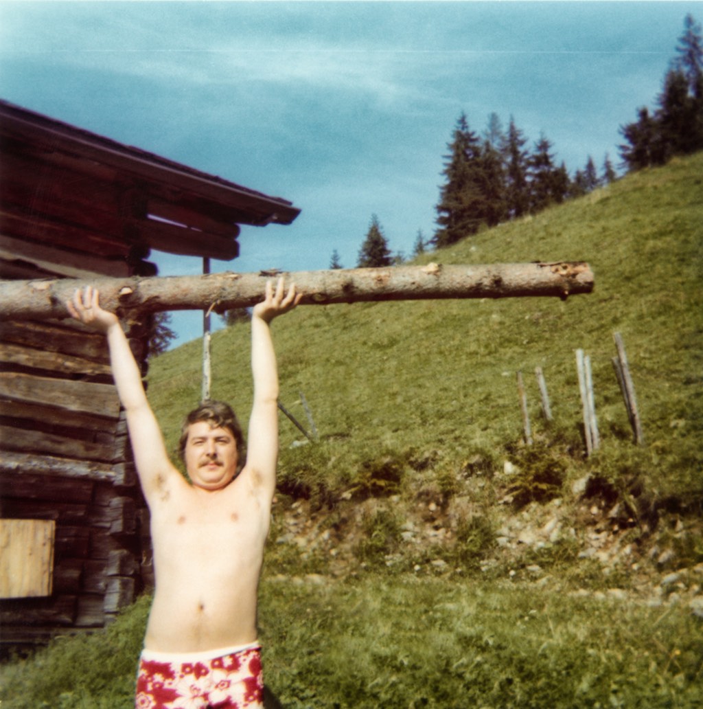 Ein junger Mann in den 70er Jahren macht Spaß und stemmt einen Baum in die Luft.